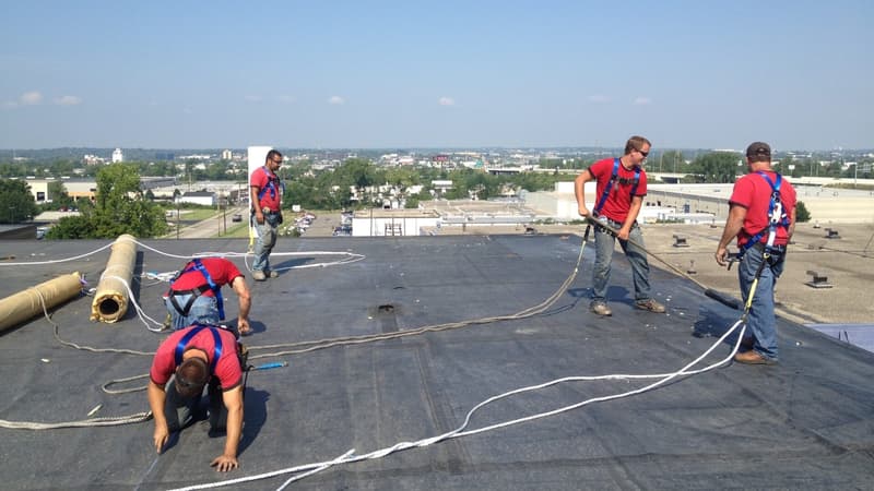 Roofing crew in safety harnesses installing membrane on a flat commercial roof
